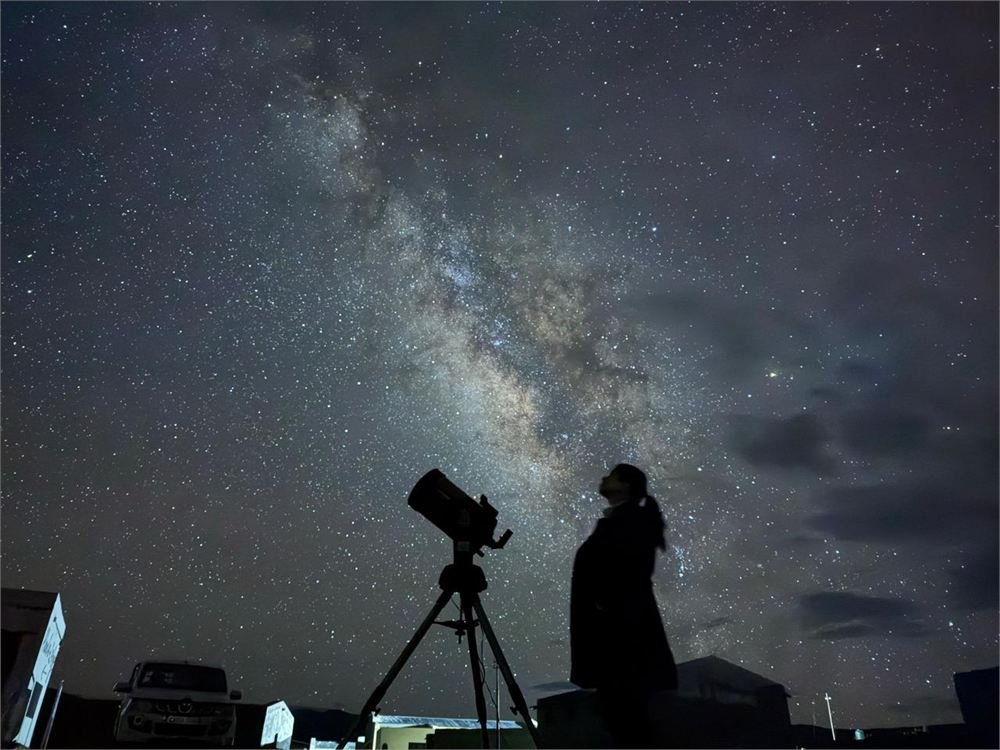 Silhouette of a person beside a telescope looking up at the Milky Way's galactic core